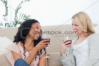 Two women sitting on the floor are talking and drinking wine
