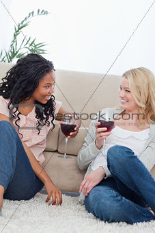 Two women are sitting on the ground leaning against a couch
