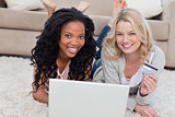 Two women are smiling at the camera with a laptop in front of th