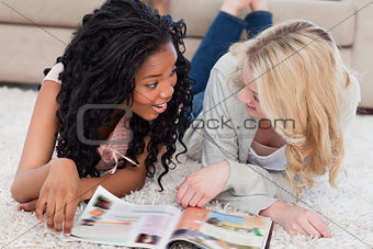 Two women are lying on the floor and talking with a magazine in 