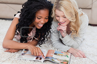 A woman is pointing at a magazine with her friend beside her