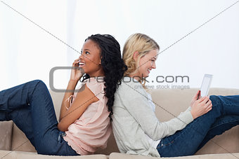 Two women sitting back to back on a couch
