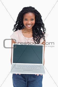 A young woman is holding a laptop out in front of her