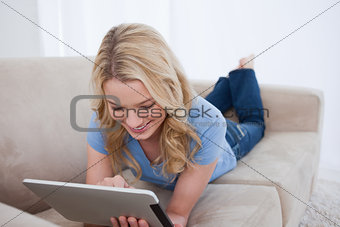A smiling woman lying on a couch is using her tablet