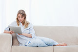 A woman sitting on a couch is using a tablet