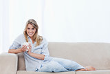 A woman holding a cup of coffee is sitting on a couch