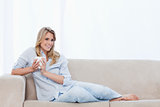 A smiling woman lying on a couch is holding a cup of coffee