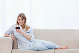A smiling woman lying on a couch is holding a glass of wine