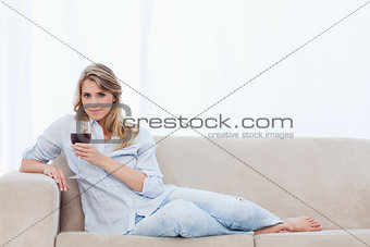 A woman looking at the camera is holding a glass of red wine