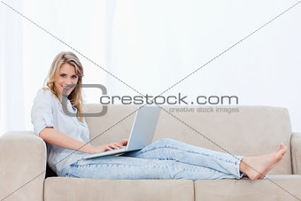 A woman lying down on a couch has a laptop on her legs