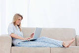 A woman is lying on a couch typing on her laptop