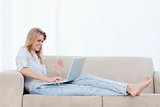 A happy woman sitting on a couch is using her laptop