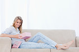 A smiling woman lying on a couch is holding a pink box