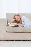 A woman lying on a couch resting her head on her hand is reading