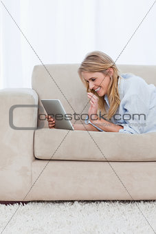 A woman lying on a couch holding a tablet is laughing