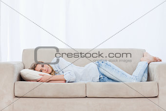 A woman is lying on a couch resting her head on a pillow 