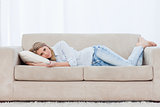 A woman holding a TV remote control is lying on a couch