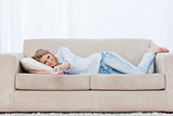A smiling woman lying on a couch is holding a TV remote control
