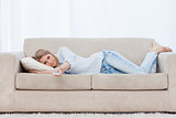 A woman lying on a couch resting is holding a television remote 