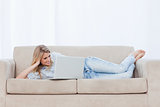 A woman lying on a couch resting her head on her hand is using h