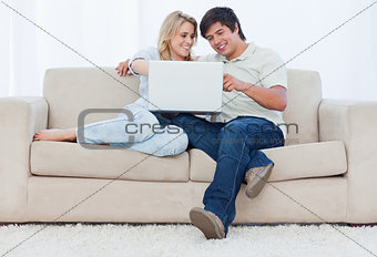 A smiling couple are sitting on a couch looking at a laptop