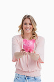 A smiling woman is holding a piggy bank in the palms of her hand