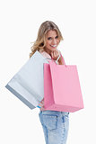 A woman looking back at the camera is carrying shopping bags ove