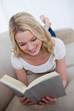 A woman lying on a couch is reading a book