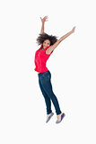 Smiling young brunette jumping while raising her arms above her 