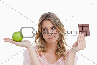 Young blonde woman hesitating between chocolate and an apple