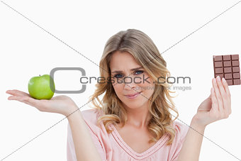 Young blonde woman holding an apple and a chocolate bar