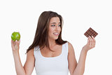 Young brunette woman holding a piece of chocolate and an apple