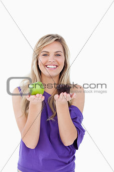 Smiling blonde woman hesitating between a muffin and an apple