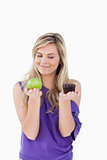 Thoughtful blonde woman holding an apple and a muffin