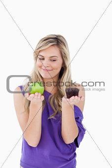 Thoughtful blonde woman holding an apple and a muffin