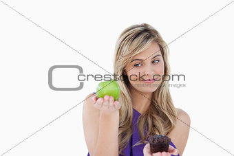 Peaceful blonde woman holding a green apple and a muffin