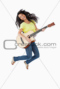 Young Latino woman holding a guitar while jumping