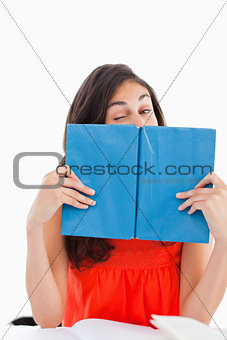 Portrait of a student winking behind a blue book