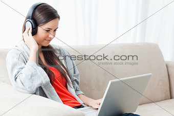 A woman on the couch with her laptop and listening to headphones