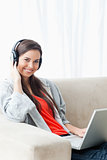 A smiling young woman using a laptop and headphones while lookin