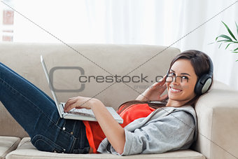 A woman looking at the camera while she uses a laptop and headph