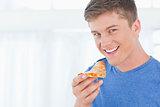 A man with a piece of pizza as he looks at the camera