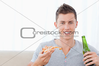 A man smiling with beer in one hand and pizza in the other