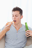 A man with a piece of pizza and some beer in his hands