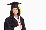 A woman standing to the side slightly with her degree and dresse