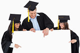 Three graduates pointing to the blank sign