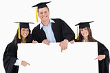 Three graduates pointing to the blank sign as they look at the c