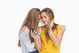 Upset young woman looking her cellphone consolded by her friend