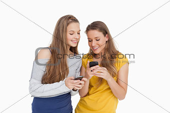 Two young women smiling while looking their cellphones