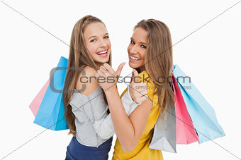Rear view of two young women the thumb-up with shopping bags